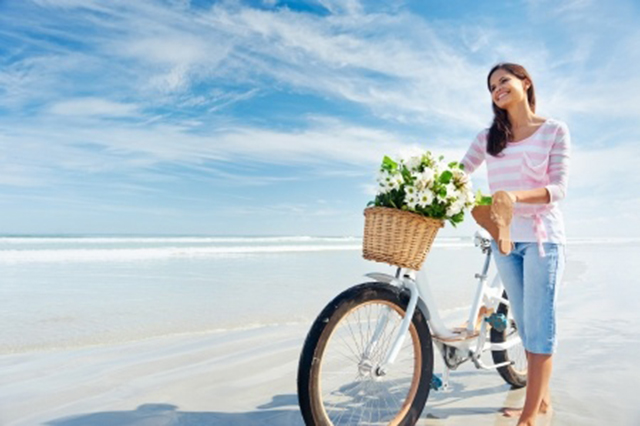 Image of young woman with bicycle on sandy beach with the ocean in the background